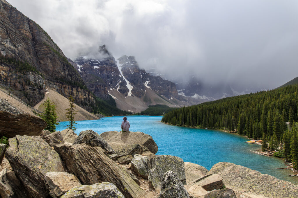 A lone girl sits on a pile of rocks overlooking Moraine Lake in Banff National Park
