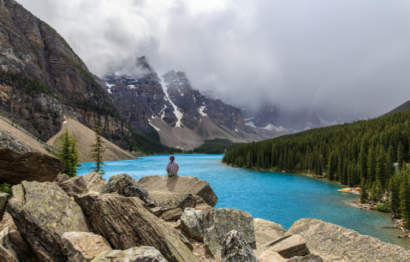 A lone girl sits on a pile of rocks overlooking Moraine Lake in Banff National Park